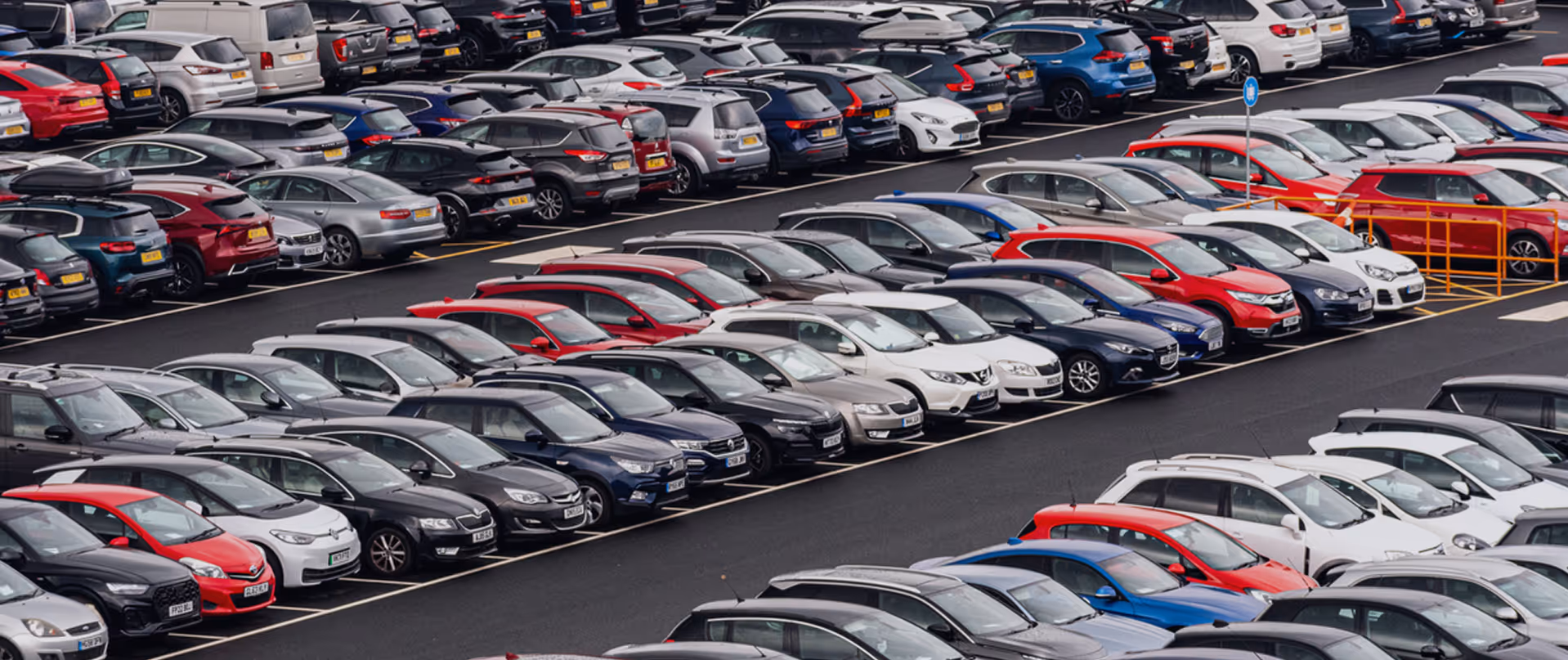 Large carpark filled with rows of various colored cars parked in marked spaces.
